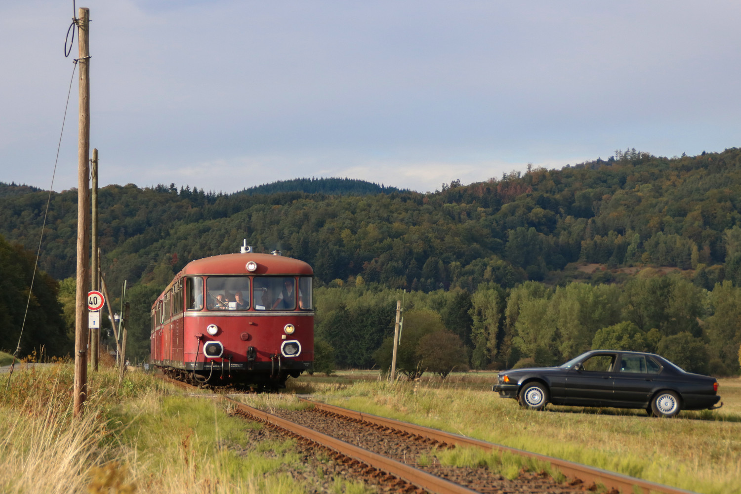 Ein schwarzer BMW wartet an einem Bahnübergang auf 798 829, 996 310, 798 589 und 998 184 in der nähe von Eckelshausen auf der oberen Lahntalbahn, aufgenommen am 09.09.2018.